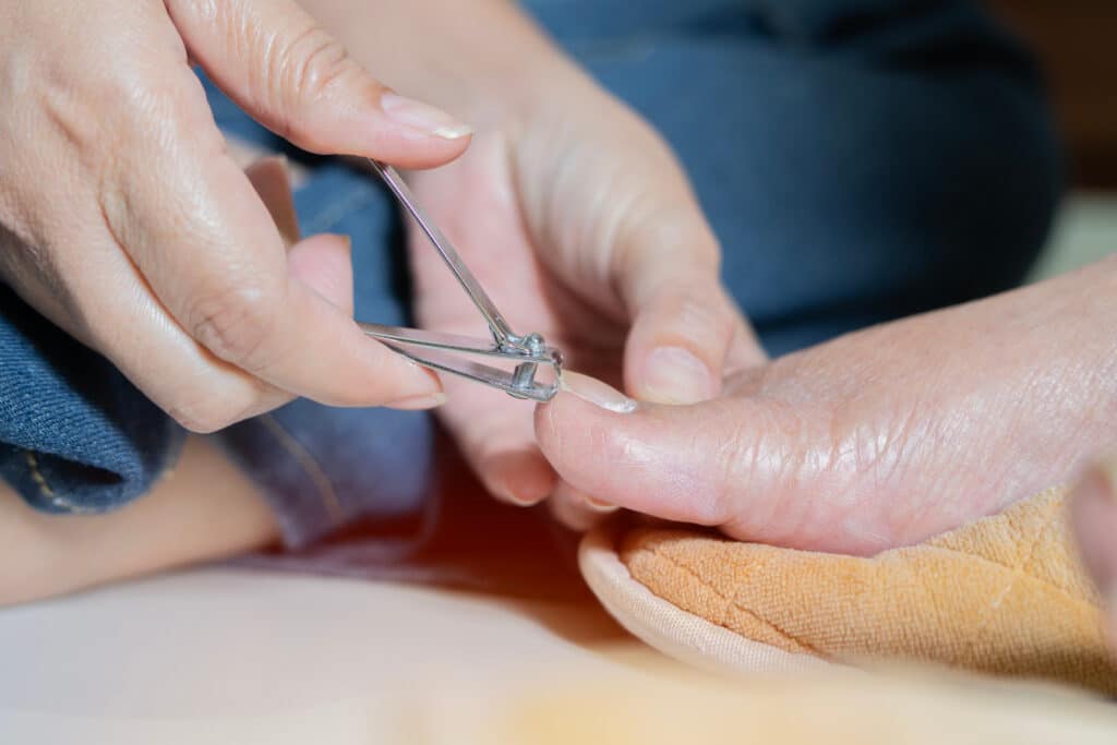 Side view close-up of old elderly on cleanliness related to the body by cutting ingrown toenails, pedicure with nail clippers, hygiene assistance in nursing home.